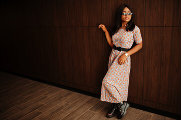 Fashion portrait of african american woman in long dress, boots and sunglasses indoor.