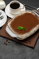 Traditional Italian Tiramisu dessert in glass baking dish and cup of fresh hot espresso coffee on concrete background