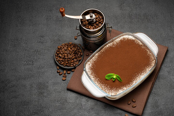 Traditional Italian Tiramisu dessert in glass baking dish and coffee grinder mill on concrete background