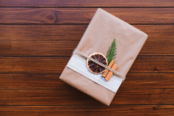 Wrapped gift box with natural decorations on brown rustic wooden background.