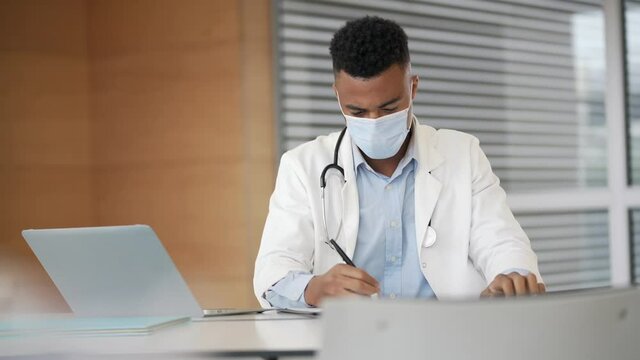 Young doctor working on laptop with face mask