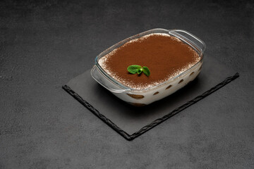 Traditional Italian Tiramisu dessert in glass baking dish on stone serving board on concrete background