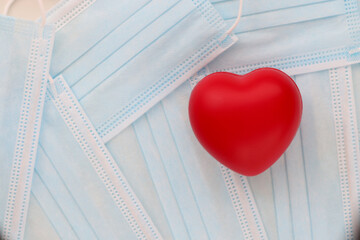 Red toy heart lying on table among medical protective masks in clinic. Complication of cardiovascular system covid-19 concept