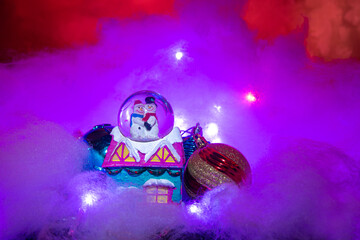 Christmas ornaments on cloud surface and colorful lights with blurred background, selective focus.