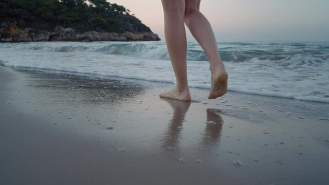 Camera follows woman walk barefoot on beautiful calm sandy beach at resort or hotel. Ocean waves surf roll over her feet. Concept tranquility and self care in peaceful setting