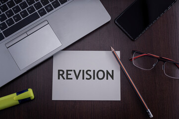 Top view of laptop, phone, glasses and pencil with card with inscription revision. Business concept.