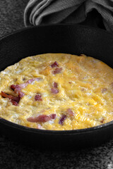 Omelette, with bacon, on a black granite surface in a cast iron frying pan.  Selective colour image