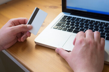 Man's hands holding a credit card and using laptop for online shopping.