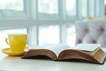 Open old book with yellow cup of coffee on the desk