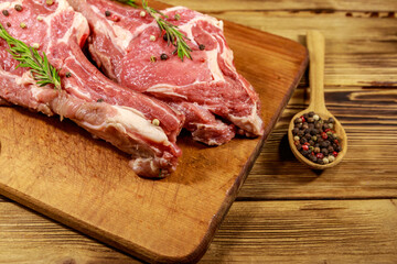 Raw fresh beef rib eye steaks on bone with spices and rosemary on wooden table