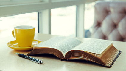 Open old book with yellow cup of coffee on the desk