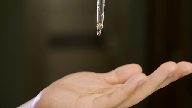 Drop of professional barber transparent liquid drips on hand against blurred dark background extreme close view slow motion