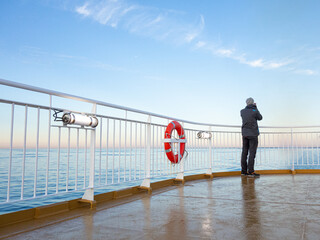 Man Standing on Ferry Deck Railing and Taking a Picture of the Sea