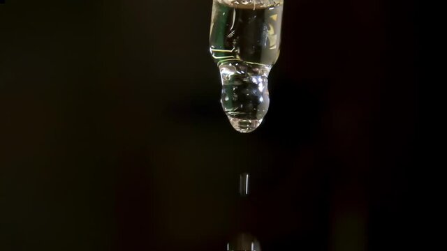 Styling liquid drop drips from transparent glass pipette against black professional studio background extreme close view