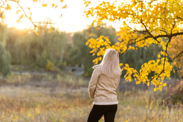 Young woman with autumn leaves in hand and fall yellow maple garden background