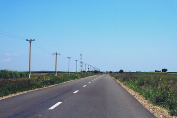 Fototapeta premium Una solitaria carretera rural en la Rumanía. Carretera de doble sentido entre campos de cultivo en un soleado día de verano.