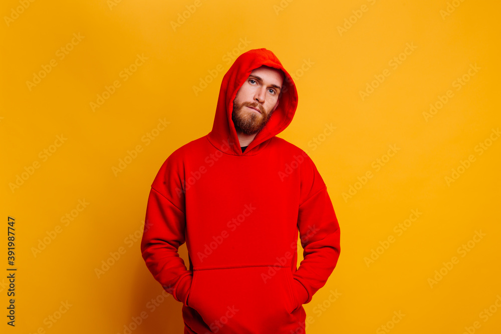 Wall mural Happy  caucasian handsome brutal bearder man wearing warm red winter trendy fleece hoodie, studio shot, yellow background.  