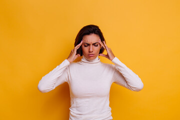 Woman suffering from headache, feeling strees. Studio shot, casual clothes, yellow background. 