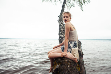 young blond woman hanging on birch tree at lake shore, summer vacations outdoor lifestyle