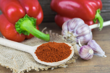Natural, organic red pepper on wooden background with 
spice on a spoon and a bunch of garlic