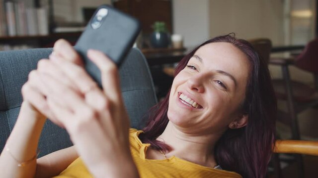 Smiling young woman lying on sofa at home looking at mobile phone - shot in slow motion 