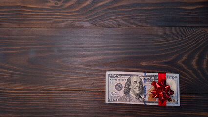 Stack Of Hundred-Dollar Banknotes gift for the new year or christmas. with red bow flat lay on a wooden background. top view