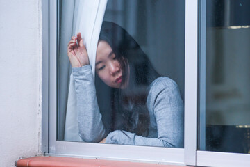 girl in stress at home - dramatic portrait of young sad and depressed Asian Korean woman on window feeling worried and desperate during covid19 stay home and lockdown