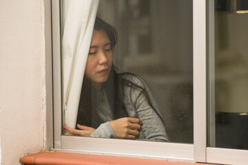 girl in stress at home - dramatic portrait of young sad and depressed Asian Chinese woman on window feeling worried and desperate during covid19 stay home and lockdown