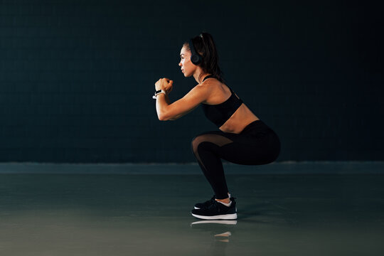 Side view of muscular woman with headphones doing squats in gym