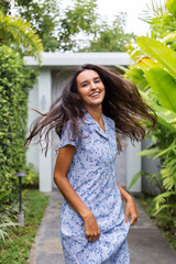 Outdoor portrait of woman long hair in dress by door, tropical location, green leaves.  