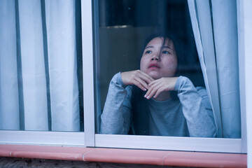 girl in stress at home - dramatic portrait of young sad and depressed Asian Japanese woman on window feeling worried and desperate during covid19 stay home and lockdown