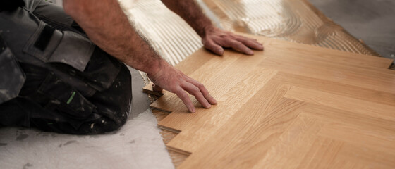 Bodenleger auf der Baustelle beim Verlegen eines Fischgräten Parkett Boden aus Eiche	

