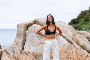 Portrait of happy slim stylish woman on rocky beach at sunset   
