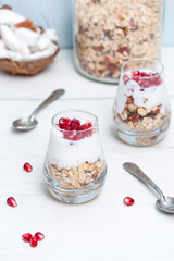 Homemade yougurt with granola and pomegranate fruit in glasses on white wooden table. Healthy breakfast.