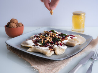 dumplings on a plate sprinkled with nuts, chocolate and decorated with fresh mint leaves, hand holding peanuts