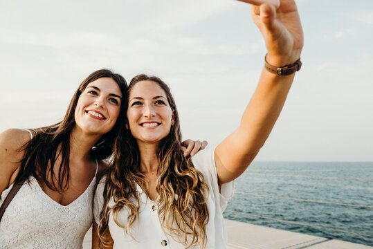 two friends take a selfie with their phone with the sea in the background
