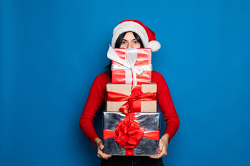 Young woman in Santa hat showing Christmas gift on blue background