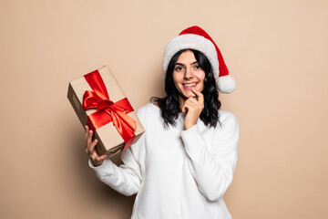 Beautiful woman hold gift isolated on beige background. Santa hat. Christmas girl portrait.