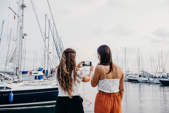 two women from behind take a photo with their mobile phone in the port