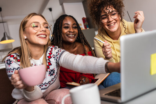 Group of multi ethnic female students learning at home using laptop and books for research.	