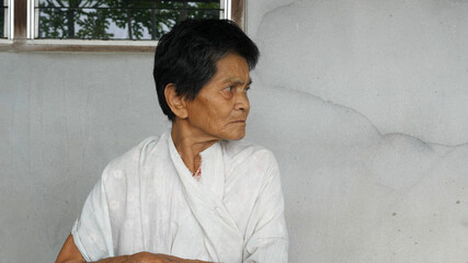 Obraz premium Asian old woman looking side way with relax face isolated concrete grey wall background. Rural lifestyle concept.