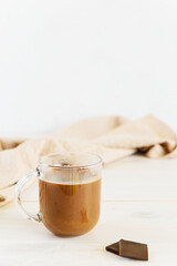 Hot chocolate with coconut milk in a glass mug on a light table.