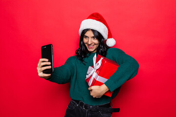 Happy pretty young woman take selfie on the phone holding gift box over red background