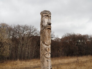 Russia, Saratov - nov,2020: Wooden idol of the Slavic God Perun near the path in the forest. Gloomy forest in the background and dark clouds