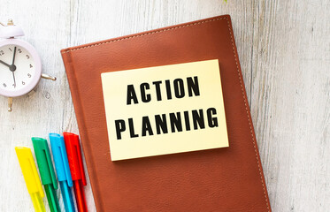 Brown notepad, sticker with the inscription ACTION PLANNING on a wooden background.