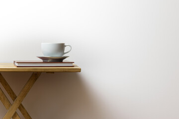 White cup of coffee on a book and on a wooden table, white background