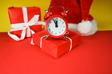 Red clock with Christmas Santa hat and gift boxes. Time for Christmas shopping concept. Blank red space for text.