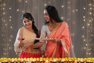 Young teen placing diyas along with her mother 	