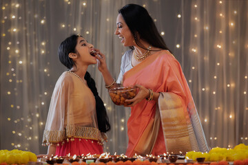 Young girl eating sweets through her mother's hand	
