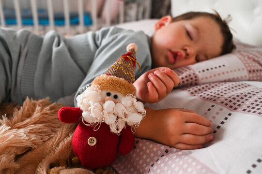 Sweet caucasian toodler boy sleeping in his bed next to a toy gnome. Christmas morning concept.